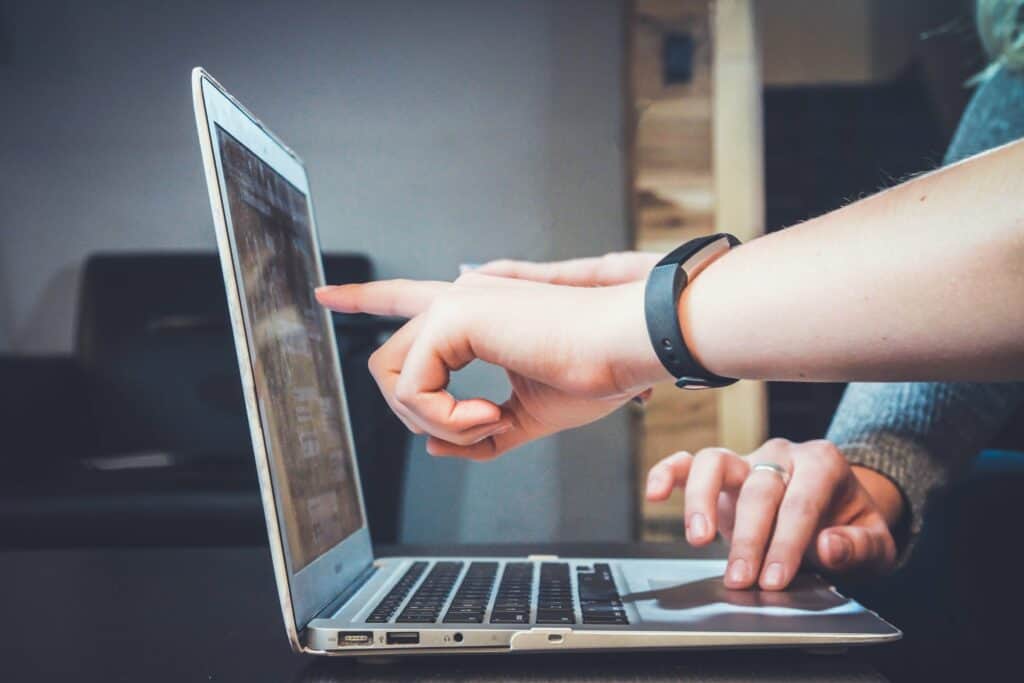a mans hand pointing to a laptop screen with another person